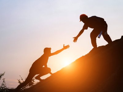 Tourists go up the hill in the sunrise to shake hands The male traveler shakes the hand of the male traveler who is climbing to the top of the hill